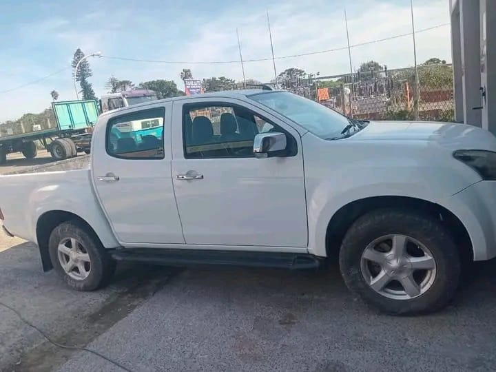 White double cab pickup truck parked beside a fence and road
